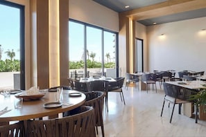 A modern dining area with round tables and chairs, large windows, and a view of greenery outside.