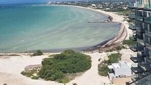 A coastal view with a beach, ocean, and a modern building with balconies overlooking the sea. - Dpto. de 2 Hab. Frente a la Playa & Amenidades Top (Progreso)