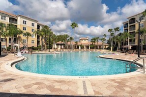 A swimming pool surrounded by lounge chairs and palm trees, with a multi-story building in the background. - GoUppers® Lakeview Condo Private Jacuzzi & Resort (Orlando)
