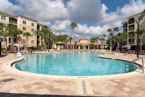 A swimming pool surrounded by lounge chairs and palm trees, with a multi-story building in the background. - Lakeview Condo Private Jacuzzi & Resort Pool (Orlando)