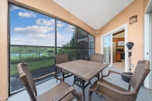 Eine Terrasse mit Tisch und Stühlen, eine Glastür, die zu einer Küche führt, und Blick auf eine grüne Landschaft.