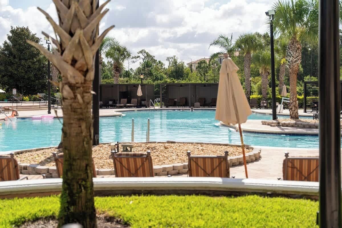 A pool area with lounge chairs and umbrellas, surrounded by palm trees and greenery.