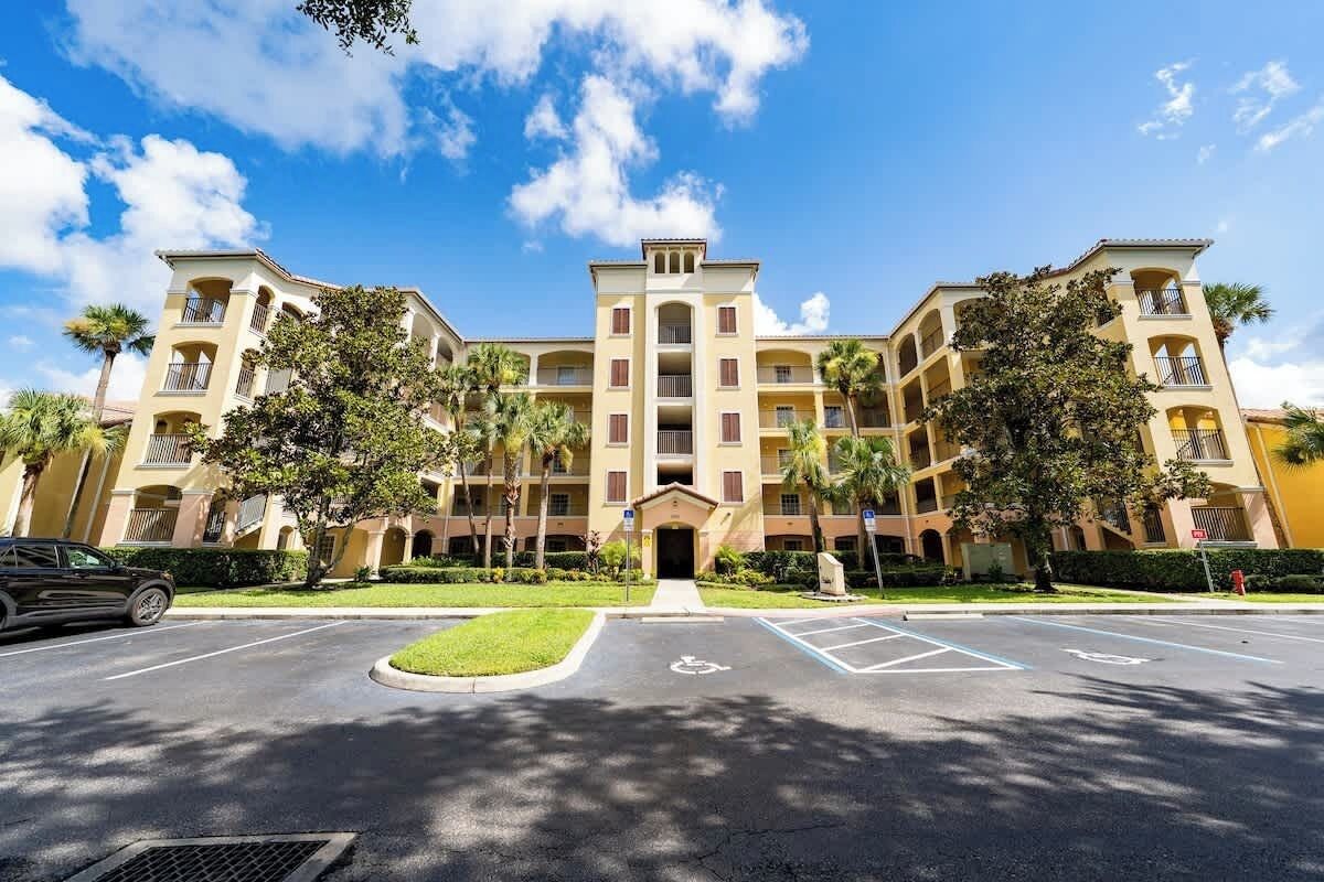 A multi-story hotel with a central entrance, parking lot, and surrounding greenery.