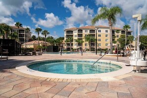 A pool area with a hot tub, lounge chairs, and a building with balconies. - GoUppers® Lakeview Condo Private Jacuzzi & Resort (Orlando)