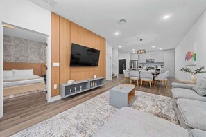A modern living room with a flat-screen TV, a sofa, a coffee table, and a dining area with chairs. - Davenport Disney Home Private Pool (Davenport)