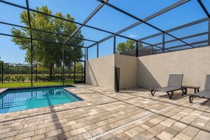 An outdoor swimming pool with a glass enclosure, surrounded by a paved patio area with lounge chairs. - Davenport Disney Home Private Pool (Davenport)