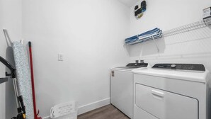 A laundry room with a washing machine, a dryer, a wall-mounted drying rack, and a laundry basket. - Davenport Disney Home Private Pool (Davenport)