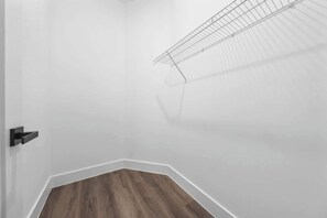 Um quarto com parede branca, chão de madeira e prateleira de metal.