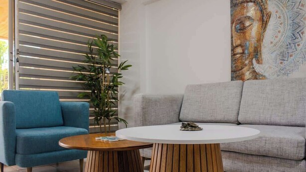 Ein modernes Wohnzimmer mit einer Couch, einem blauen Sessel, einem runden Holztisch und einem großen Buddha-Gemälde an der Wand.