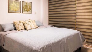 Ein Schlafzimmer mit einem großen Bett, zwei an der Wand befestigten Kunstwerken, einer Deckenleuchte und einem Fenster mit Jalousien.