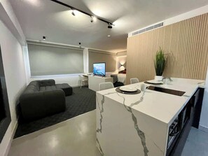 Ein modernes Hotelzimmer mit einer Marmor-Insel, einem Flachbildfernseher, einer Couch und einem Essbereich mit einer Pflanze.