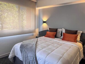 A bedroom with a bed, pillows, a blanket, a nightstand, and a wall-mounted light fixture. - Remodelado y Cómodo: Internet Rápido + Zona Top (Caracas)