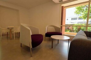 A modern lounge area with seating and a table, large windows with a view of greenery and buildings. - Remodelado y Cómodo: Internet Rápido + Zona Top (Caracas)