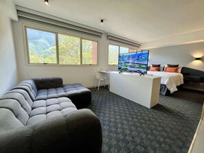 A hotel room with a large sofa, a desk, a bed, and a TV.