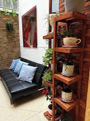 A cozy room with a black sofa, a wooden shelf with potted plants, and a brick wall. - Villa Suites en Chapinero Alto (Bogotá)