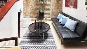 Una sala de estar moderna con un sofá de cuero negro, alfombra estampada y una mesa redonda de centro con jarrones.