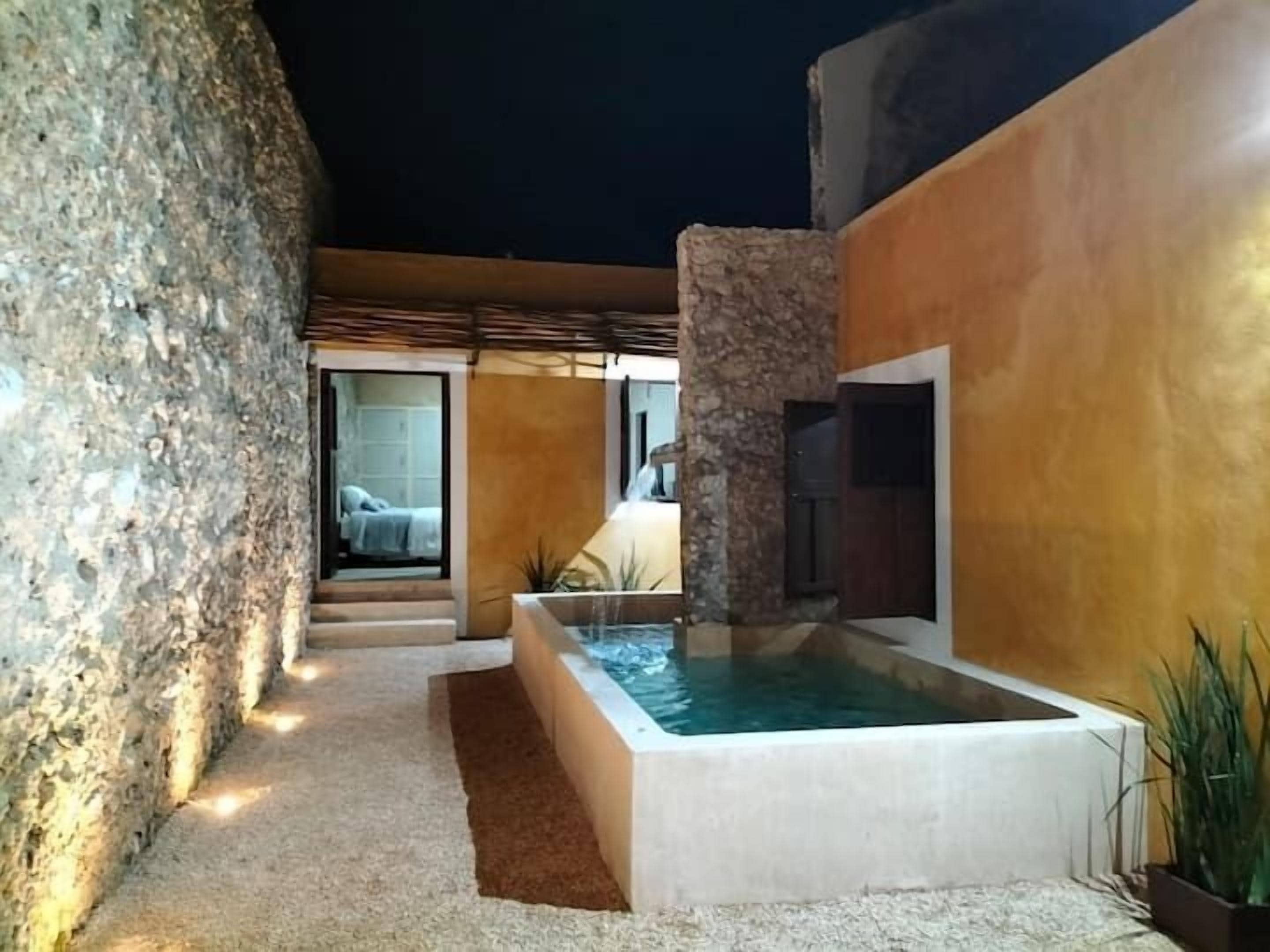 A modern outdoor pool area with a stone wall, a rectangular pool, and a covered seating area.