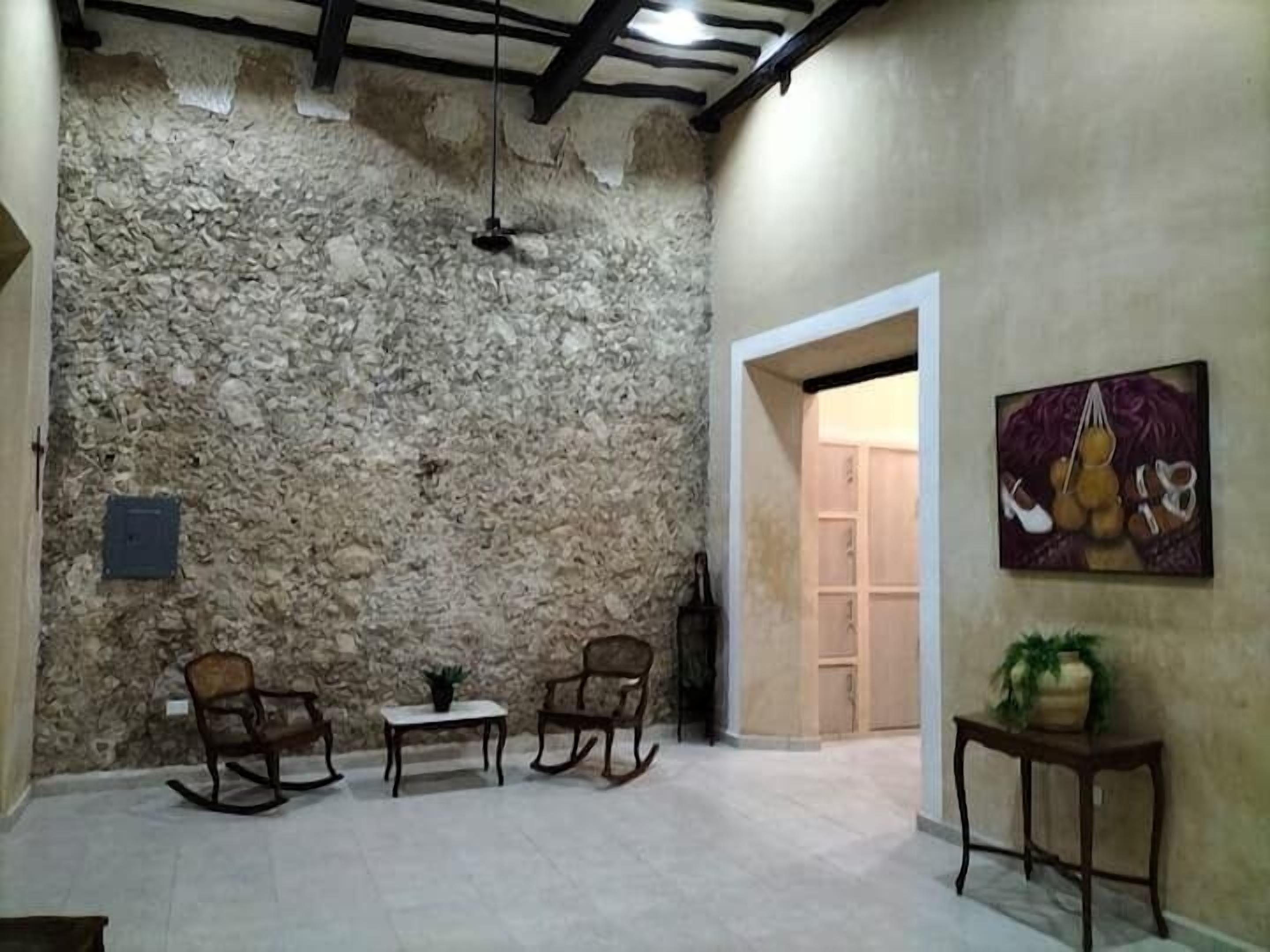 Une pièce avec un mur en pierre, un ventilateur de plafond, une table avec des chaises et un tableau accroché au mur.