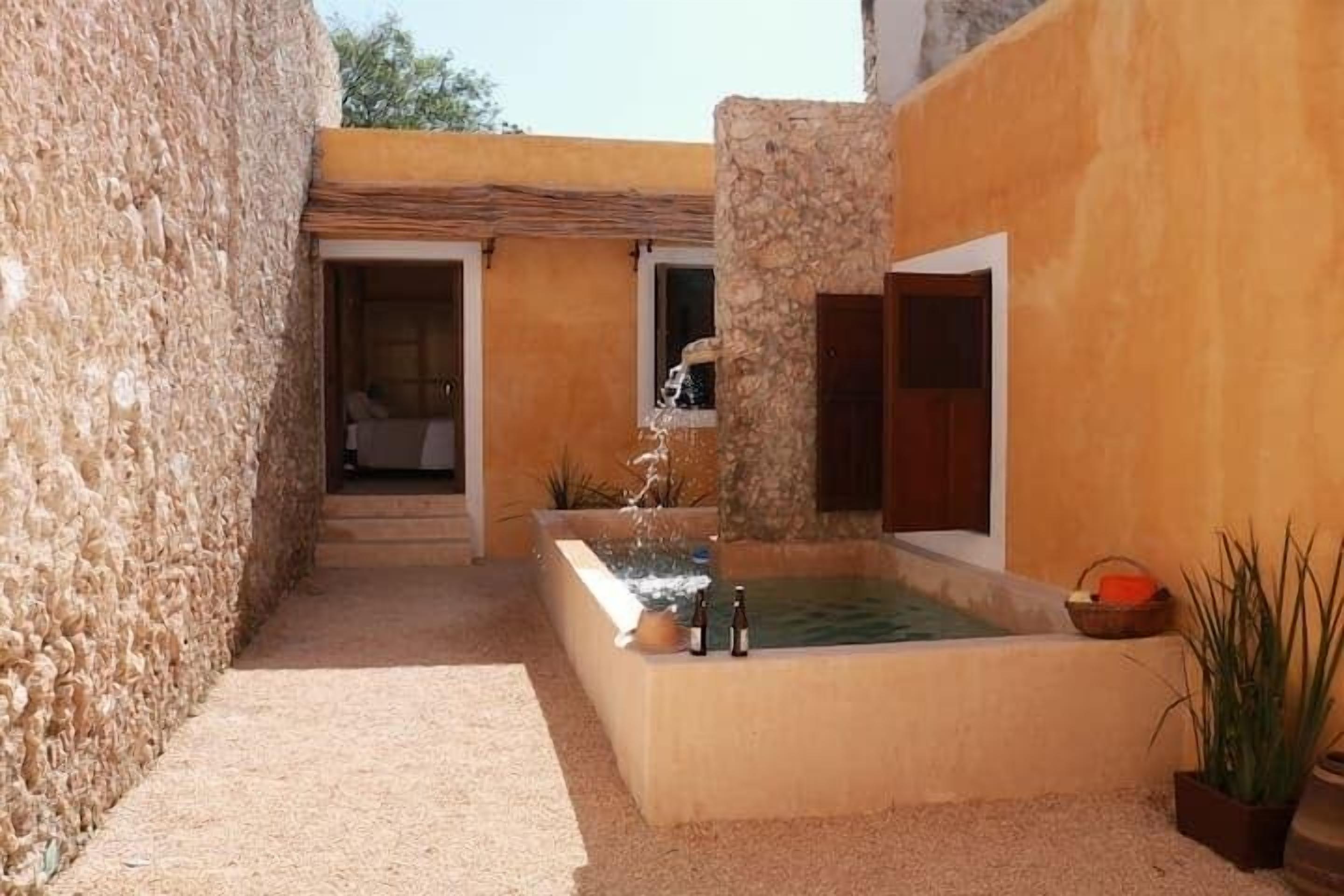 A courtyard with a water feature, a stone wall, and a building with a window.