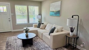 Ein Wohnzimmer mit einem Ecksofa, einem runden Couchtisch, einer Stehlampe und einem Gemälde an der Wand.