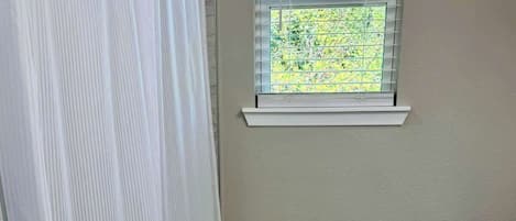 Ein Badezimmer mit Toilette, einem Fenster mit Blick auf Grünflächen, einer Duschvorhang und einem Teppich auf dem Boden.