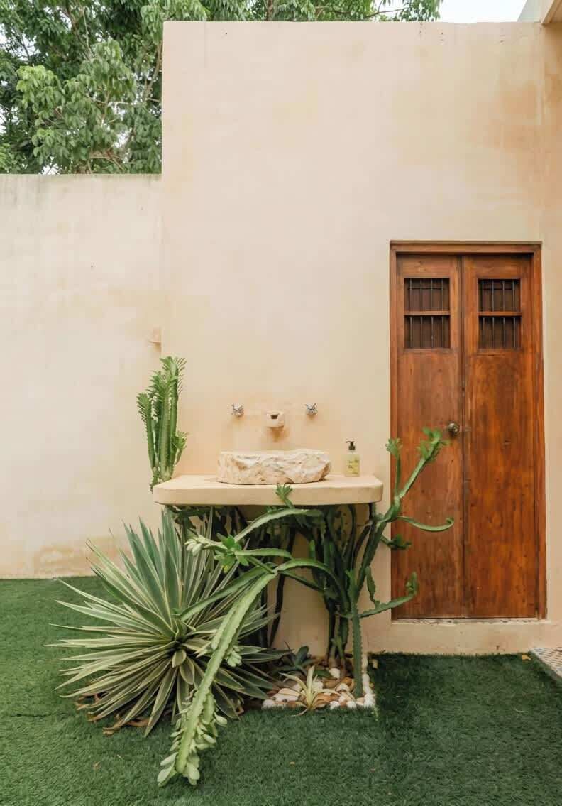 Une petite salle de bain extérieure avec un lavabo, une porte en bois et diverses plantes.