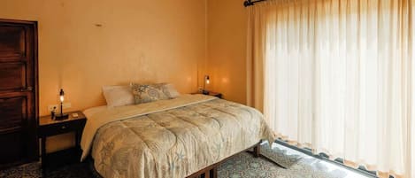 A bedroom with a bed, nightstands, a window with curtains, and patterned floor tiles.