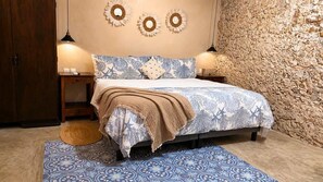 A bedroom with a bed, two bedside tables, a wall clock, and a stone wall. - La María House: lux, comfort, and pool (Merida)