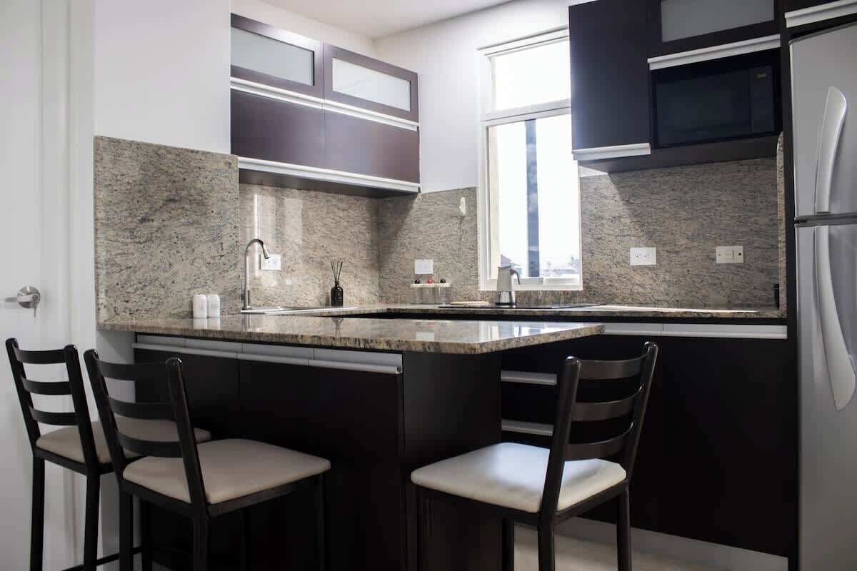 A kitchen with a granite countertop, dark cabinetry, and two bar stools.