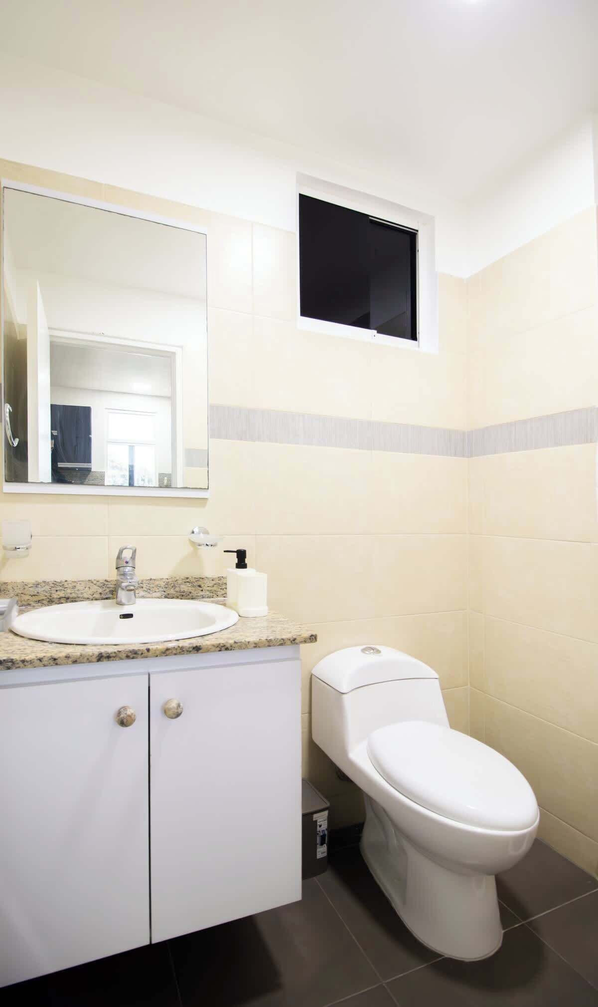 Ein Badezimmer mit einem weißen Waschbecken, einem Spiegel, einer Toilette und einem kleinen Fenster.