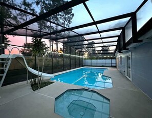 An outdoor swimming pool with a slide, surrounded by a covered area with a view of trees. - Altamonte Springs Apt: Pool & City Views, Prime (Altamonte Springs)