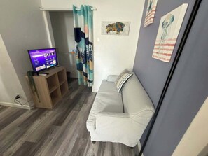 A living room with a sofa, a TV on a stand, a wooden shelf, and a wall with two artworks. - Altamonte Springs Apt: Pool & City Views, Prime (Altamonte Springs)
