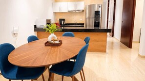 Eine moderne Küche mit Edelstahlgeräten, ein Essbereich mit einem runden Holztisch und blauen Stühlen sowie eine kleine Kochinsel mit einer Vase und einem Korb.