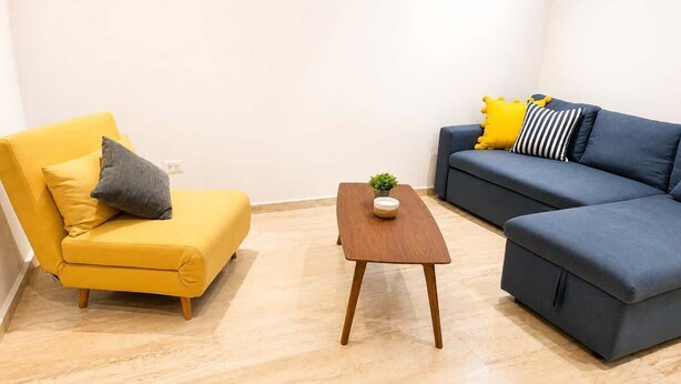 A living room with a yellow sofa, a blue sofa, and a wooden coffee table. - Acogedor departamento alberca y estacionamiento (Merida)