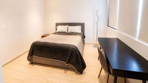 A bedroom with a bed, bedside table, and a desk. - Acogedor departamento alberca y estacionamiento (Merida)