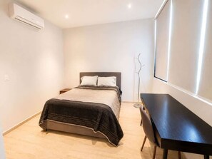 A bedroom with a bed, bedside table, and a desk. - Acogedor departamento alberca y estacionamiento (Merida)