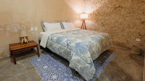 A bedroom with a bed, a nightstand, a lamp, and a patterned rug. - Casa Colonial c/Alberca Privada (Merida)