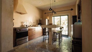 A kitchen with a stove, sink, and bar stools. - Casa Colonial c/Alberca Privada (Merida)