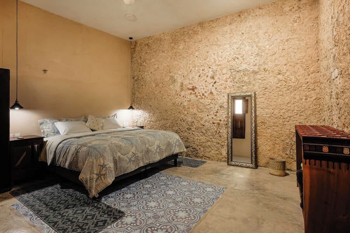 A bedroom with a bed, bedside lamps, a mirror, a rug, and a wooden dresser.