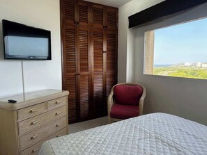 Ein Schlafzimmer mit Bett, Kommode, Fernseher, Kleiderschrank und einem Fenster mit Blick.