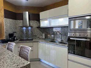 Eine moderne Küche mit Granit Arbeitsplatten, Edelstahlgeräten und weißen Schränken.