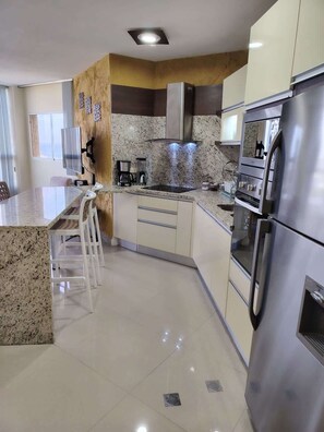 A modern kitchen with a central island, stainless steel appliances, and a flat-screen TV. - Vista al Mar - Bahia de Bella Vista (Porlamar)