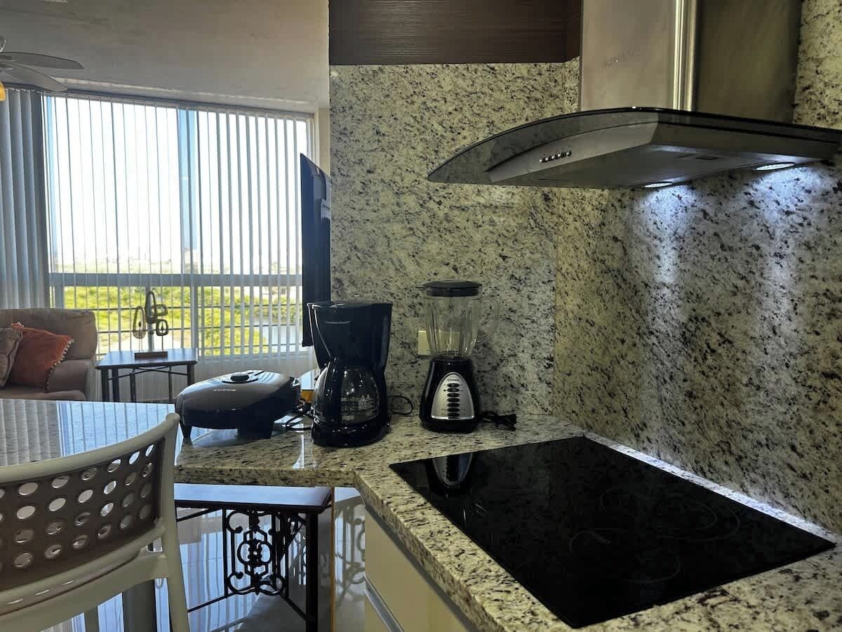A kitchen with a granite countertop, a coffee maker, a blender, and a stove.