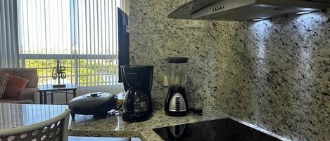 A kitchen with a granite countertop, a coffee maker, a blender, and a stove.