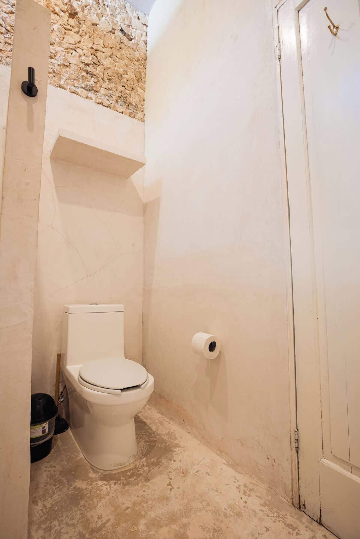 Une petite salle de bain étroite, avec des toilettes, un rouleau de papier toilette et une porte.