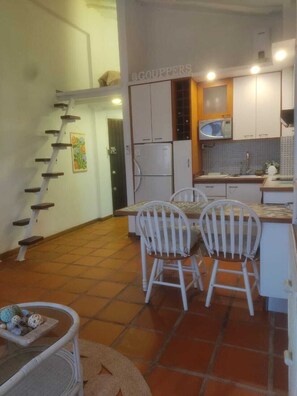 A kitchen with white cabinets, a microwave, and a dining area with two chairs. - Cozy apartment | Playa Moreno | The Beach House (Pampatar)