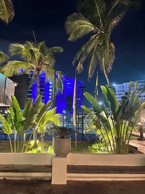 A night scene with palm trees and a building with blue lighting. - Cozy apartment | Playa Moreno | The Beach House (Pampatar)