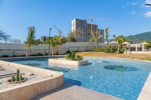 A swimming pool with a surrounding deck, palm trees, and a distant building under construction. - Santa Marta Vista Mar Playa Privada (Santa Marta)
