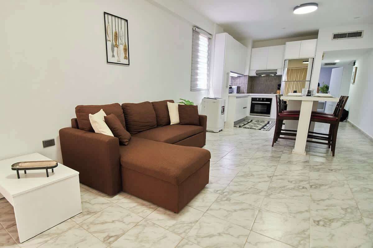 Ein modernes Wohnzimmer mit einem braunen Ecksofa, einem weißen Couchtisch und einem Essbereich mit Tisch und Stühlen.