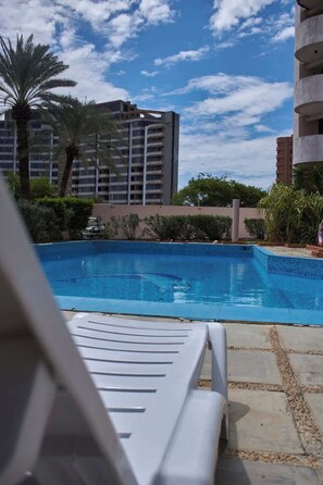 Una piscina con sillas de descanso, rodeada de palmeras y edificios.